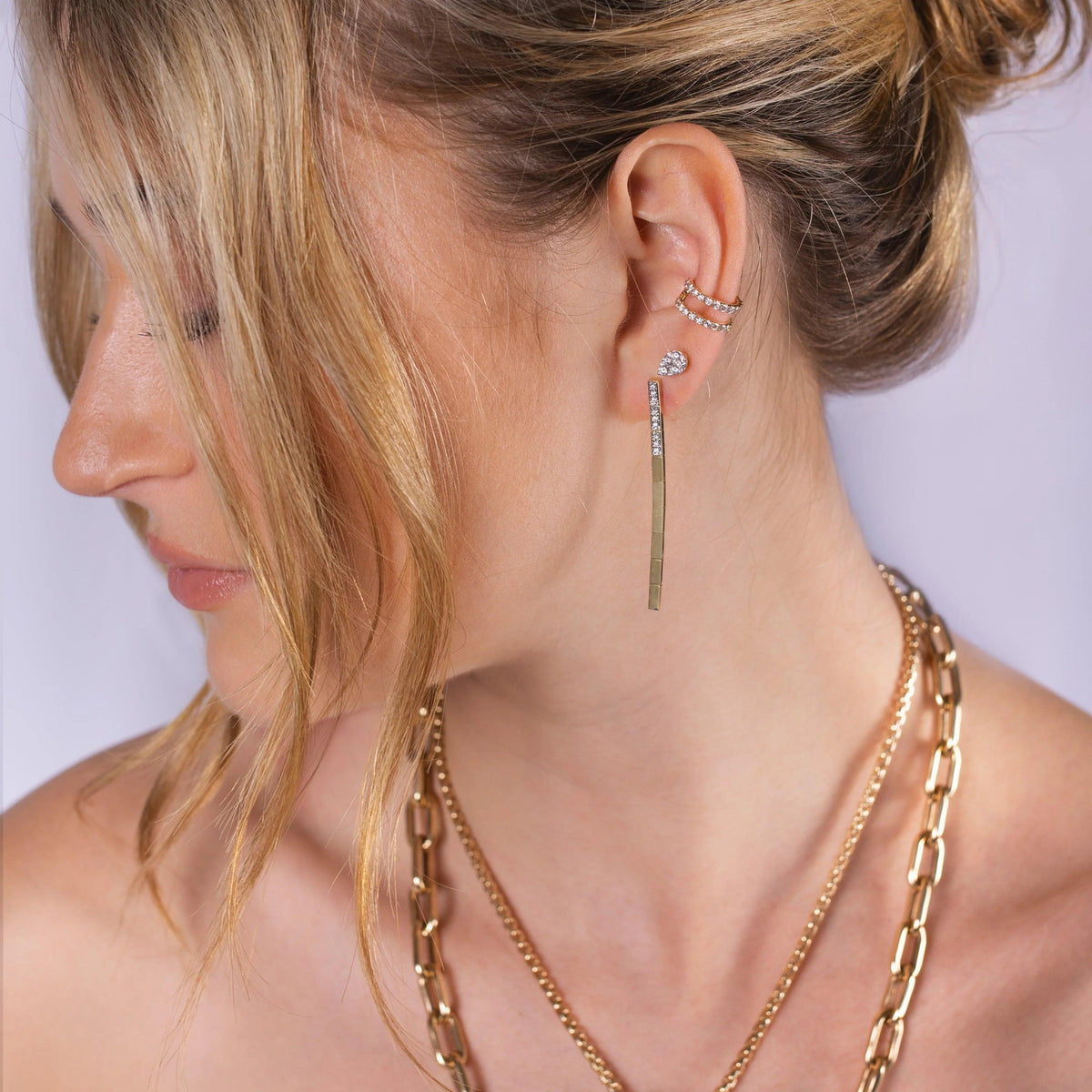 Close-up of a person wearing Gold & Diamond Serpent Earrings, Illusion Teardrop Studs, and the Open Bar Diamond Ear Cuff