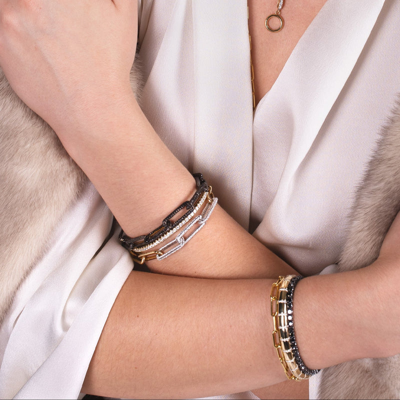 Close-up of a person wearing the 3mm Diamond Stretch Tennis Bracelet, the Black Diamond Infinity Bracelet, the Timeless Bracelet, the Diamond Section Stretch Bracelet, and the Infinity Diamond Link Bracelet. 