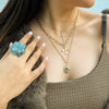 Woman is wearing the Aquamarine Pom Pom Ring, the Bezel-set Diamond Cross Necklace, the Floral Necklace, and the Labradorite Sunburst Necklace
