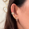Close-up of an ear wearing multiple 14K gold and diamond earrings (Chandelier Ear Cuff, Chubby Huggies, and Luxe Open Bar Diamond Huggies) with a blurred background.
