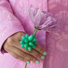 Hand holding a green Chrysoprase Pom Pom Ring with a pink flower against a pink floral background