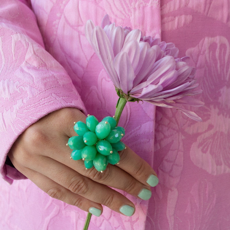 Hand holding a green Chrysoprase Pom Pom Ring with a pink flower against a pink floral background