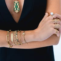 Close up of arm wearing the Diamond Arrow ID Bracelet, the Emerald Baguette & Diamond Bangle, the Timeless Bracelet, the Prism Tennis Bracelet, and the Halo Illusion Bracelet