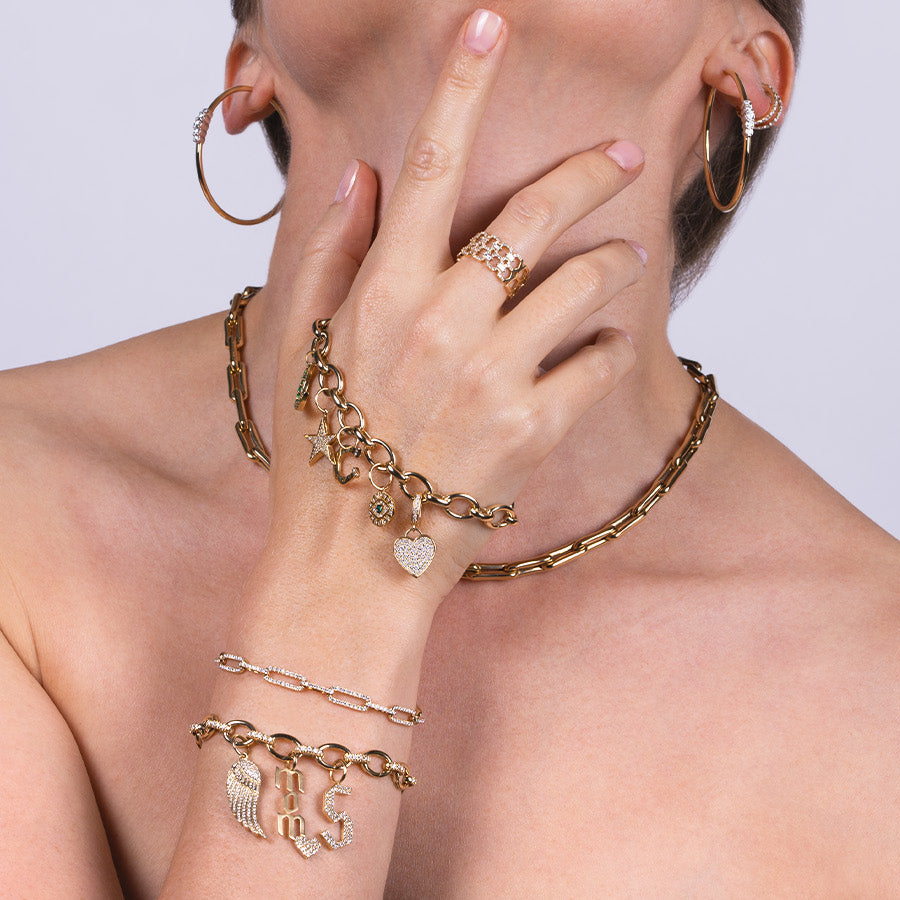 a person wearing the Diamond Oval Link Charm Bracelet with Charms, Oval Link Charm Bracelet with Charms, the Sabrina Diamond Bracelet, the Deco Status Ring, and the Bone Link Chain.
