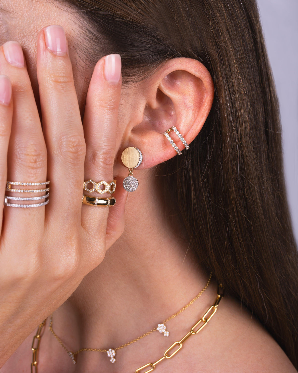 Close-up of an ear with the Eclipse Drops, Open Bar Diamond Ear Cuff, the Diamond Section Stretch Ring, the Prism Stackable Ring, and the Open Bar Diamond Rings.