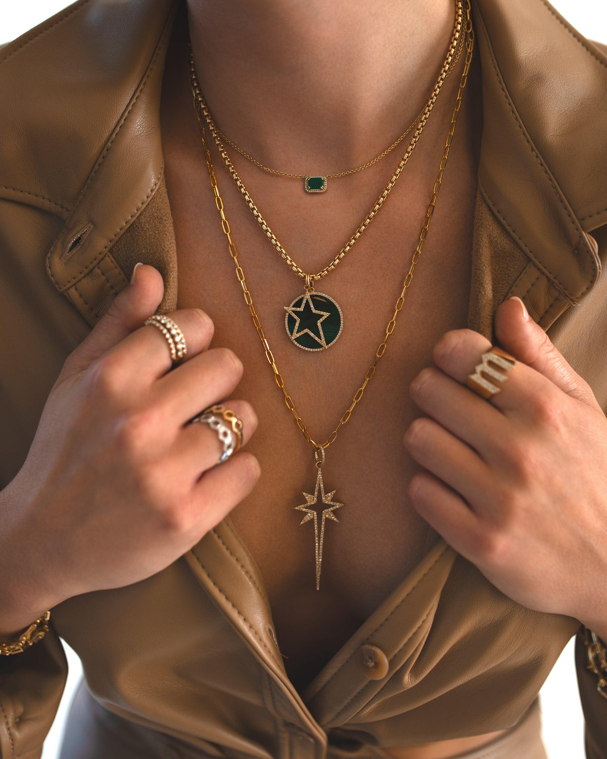 Close-up of a person wearing the Emerald Necklace, the Large Starburst Diamond Necklace, and the Large Malachite Medallion & Hollow Diamond Star Charm necklace with 3mm Box Chain