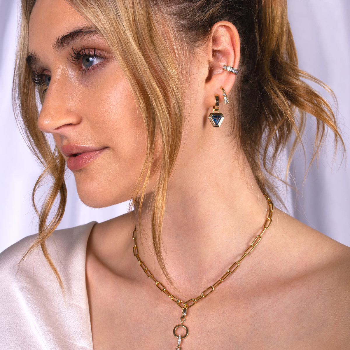 Close-up of a woman wearing the Fringe Huggies, Baguette Diamond Ear Cuff, Double Bezel London Blue Topaz Trillion Drops, Timeless Choker.