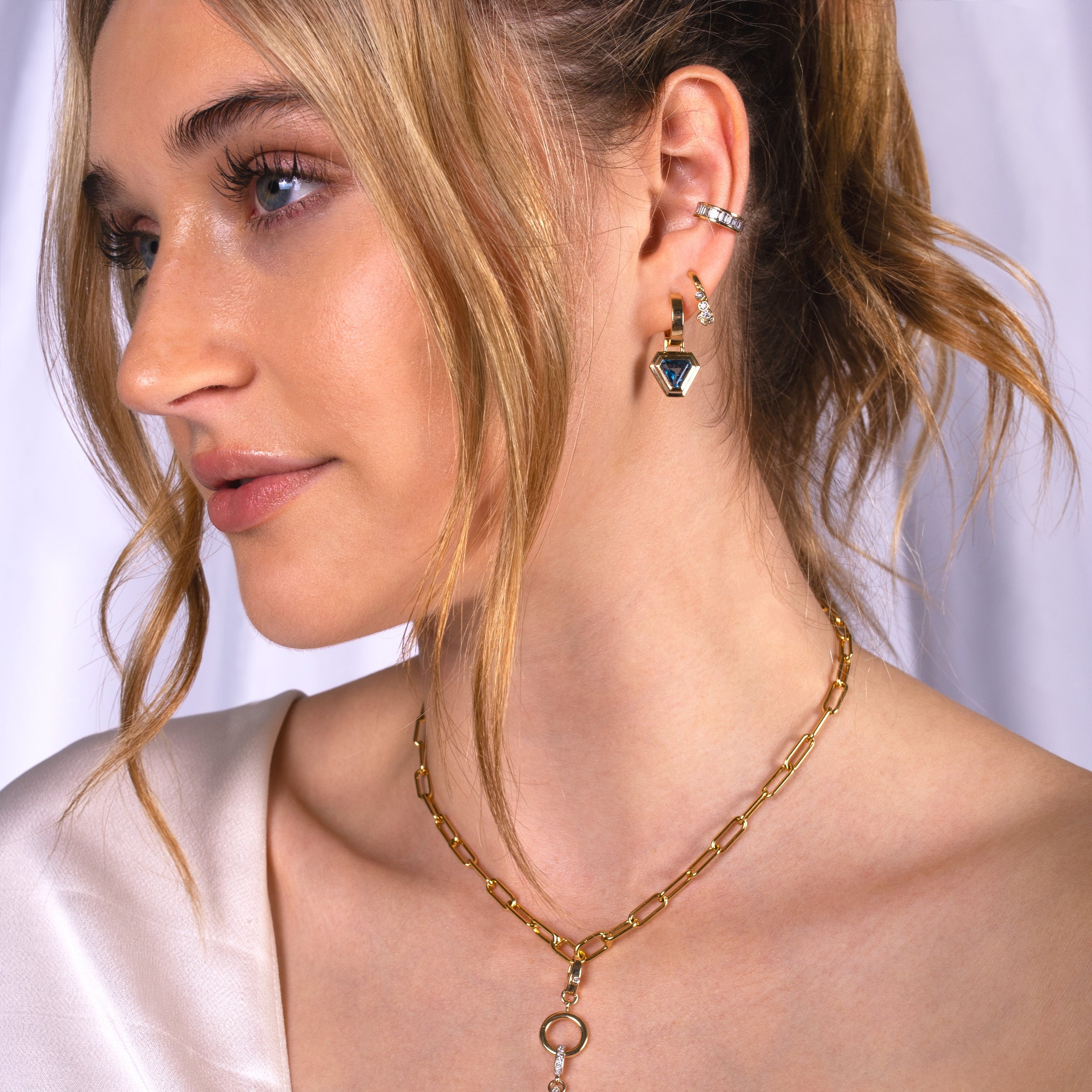 Close-up of a woman wearing the Fringe Huggies, Baguette Diamond Ear Cuff, Double Bezel London Blue Topaz Trillion Drops, Timeless Choker.
