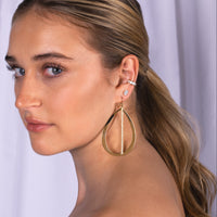 Close-up of a woman wearing Illusion Oval Studs, Baguette Diamond Ear Cuff, and Large Stackable Teardrops & Diamond Stick Earrings
