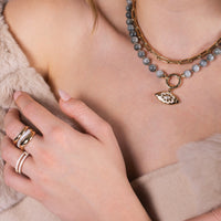 Close-up of a person wearing the Luxe Open Bar Diamond Ring, the Forever Ring, the Floral Evil Eye Eagle Eye Necklace