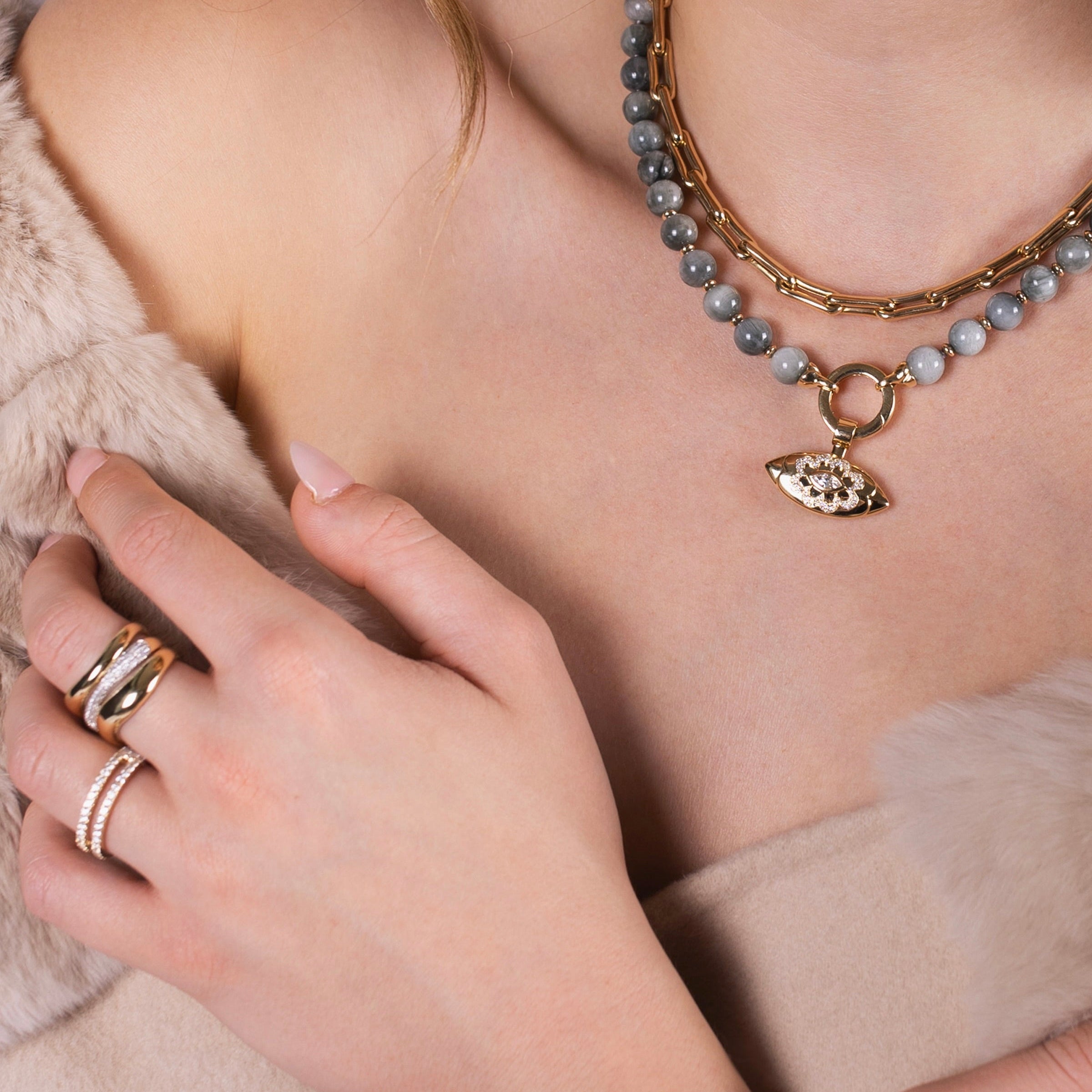 Close-up of a person wearing the Luxe Open Bar Diamond Ring, the Forever Ring, the Floral Evil Eye Eagle Eye Necklace