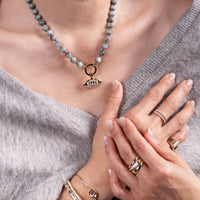 Close-up of a person wearing the Luxe Open Bar Diamond Ring, the Forever Ring, the Floral Evil Eye Eagle Eye Necklace, and the b Diamond Signet Ring