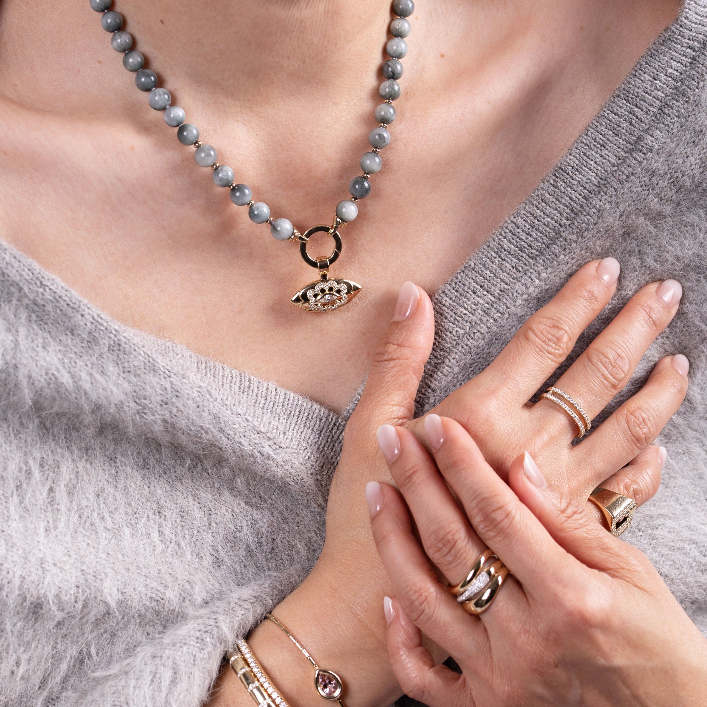 Close-up of a person wearing the Luxe Open Bar Diamond Ring, the Forever Ring, the Floral Evil Eye Eagle Eye Necklace, and the b Diamond Signet Ring