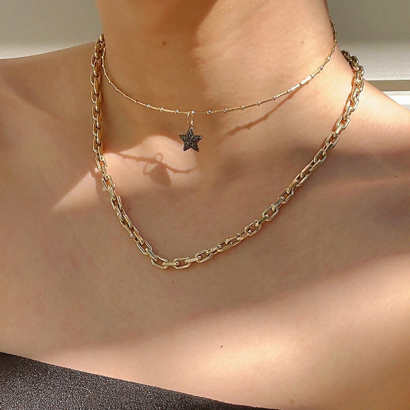 The Open Ended Choker with the Double-sided Puffy Star pendant and the Chubby Diamond Cut Chain on a person's neck