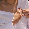 Person wearing a white off-shoulder top with the Pearl Pom Pom Ring, Liquid Vine Choker, and Pearl Row with Clasp Necklace attached to the Sunburst Pendant