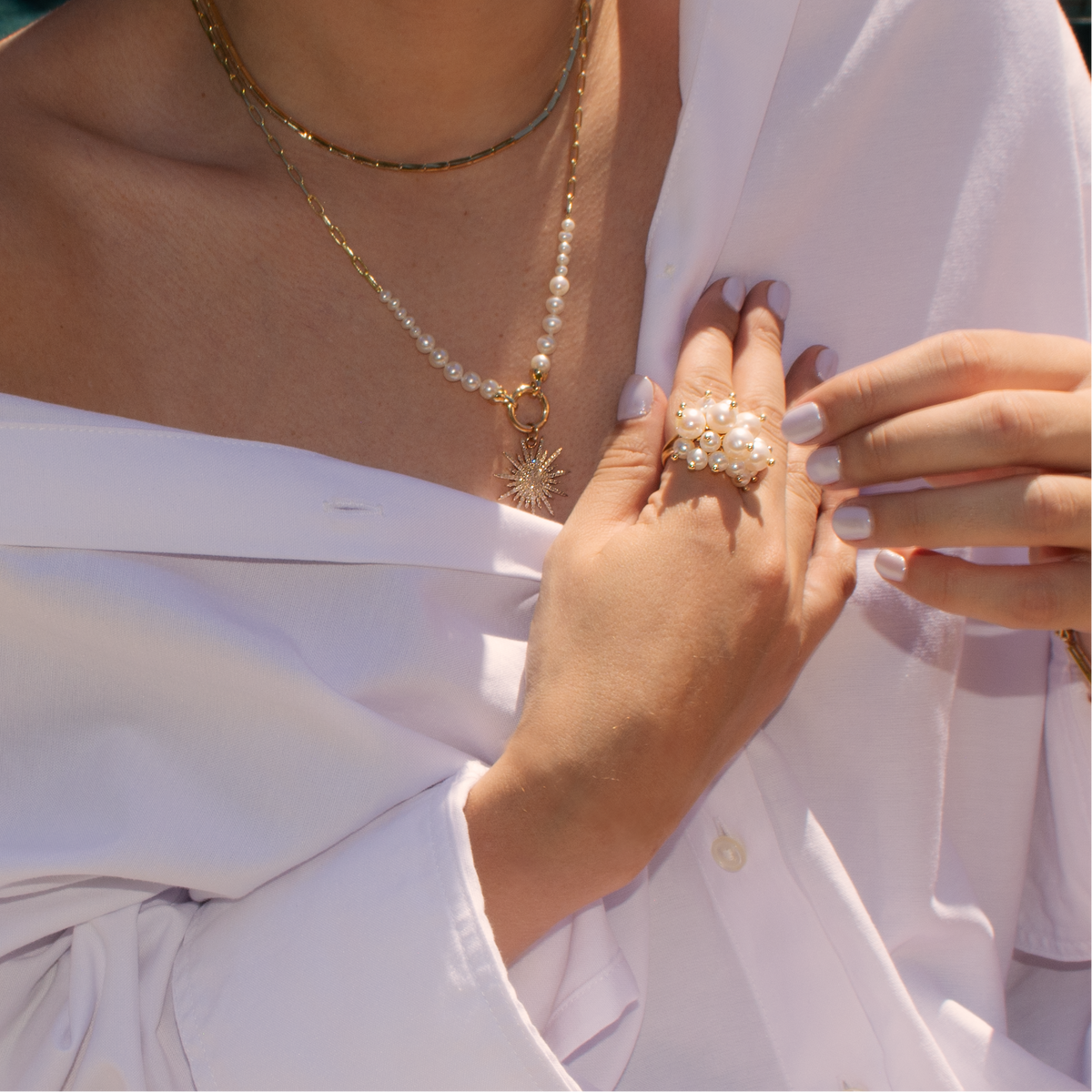 Person wearing a white off-shoulder top with the Pearl Pom Pom Ring, Liquid Vine Choker, and Pearl Row with Clasp Necklace attached to the Sunburst Pendant