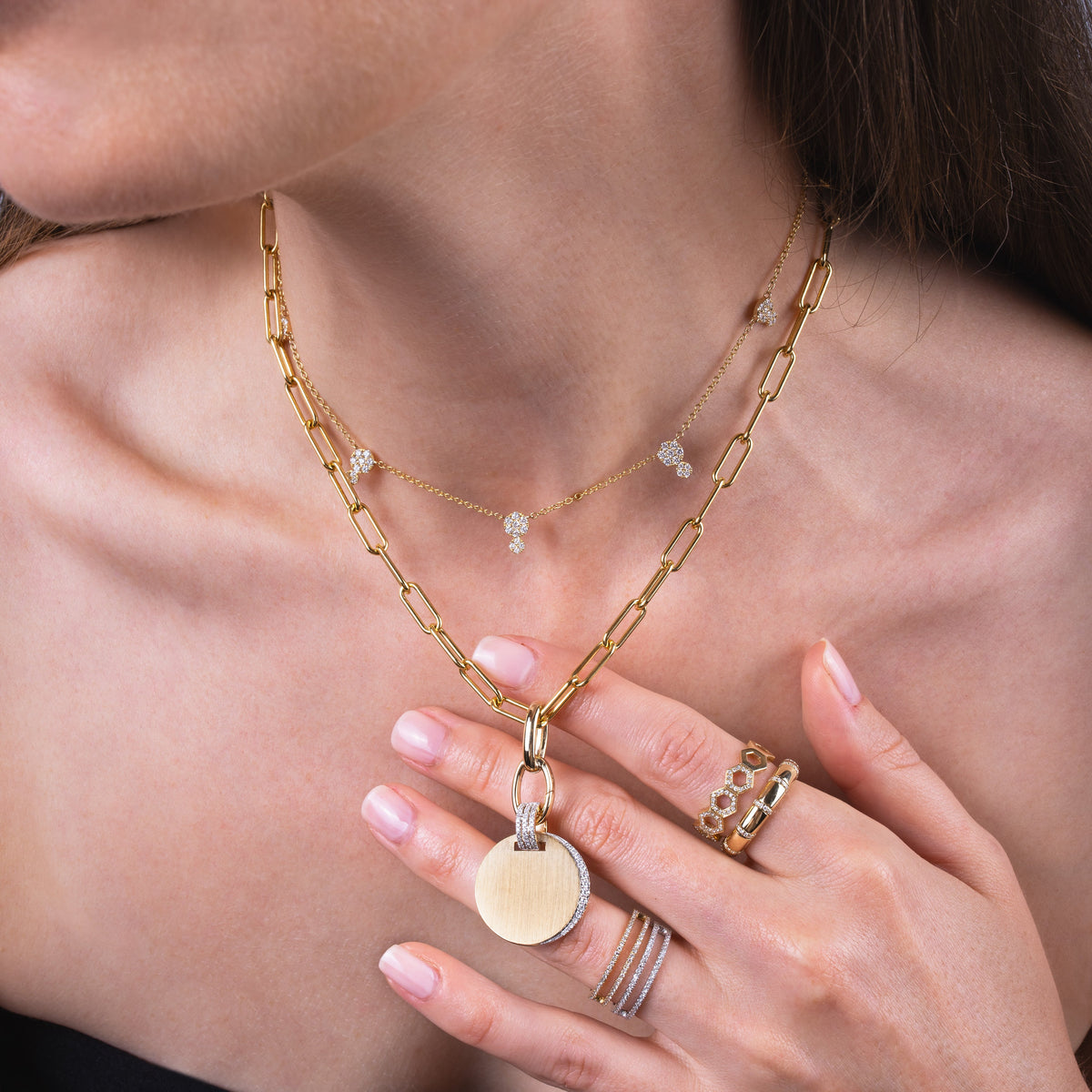 Close-up of a person wearing the Timeless Necklace with the Large Oval Double-linked Charm clasp and the White Diamond Eclipse Pendant, the Double Dot Necklace, the Open Bar Diamond rings, the Diamond Section Stretch Ring, and the Prism Stackable Ring. 