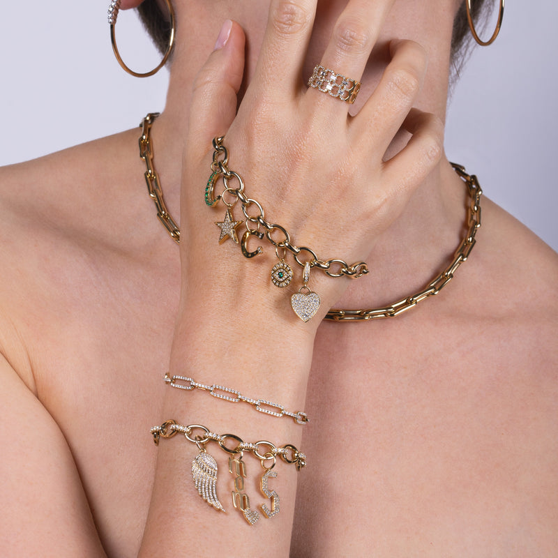 Close-up of a person wearing the Diamond Oval Link Charm Bracelet with Charms, the Oval Link Charm Bracelet with Charms, the Sabrina Bracelet, the Deco Status Ring, and the Bone Link Chain.