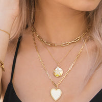 A woman wearing the Diamond Star Medallion Necklace, the Timeless Necklace, and the Enamel Heart Necklace