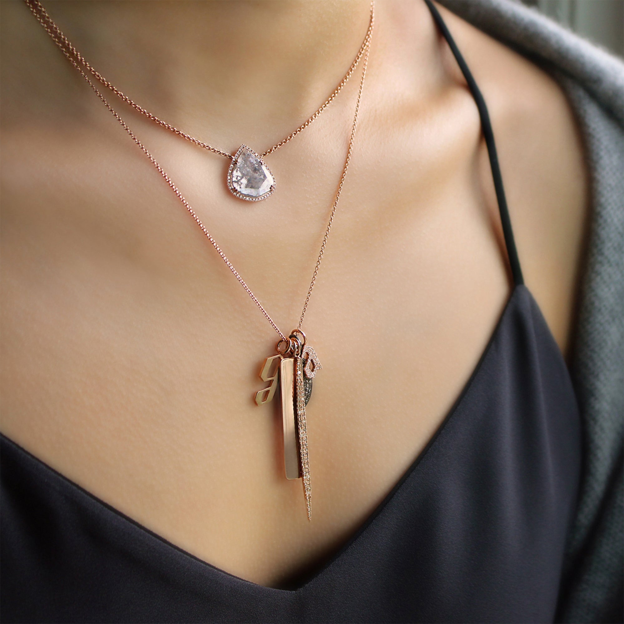 close up of woman wearing a charm necklace that includes the Dog Bone Pendant, the Small Alphabet Pendant, the Small White Diamond Alphabet Pendant, and the 2-inch Pave Diamond Spear Pendant