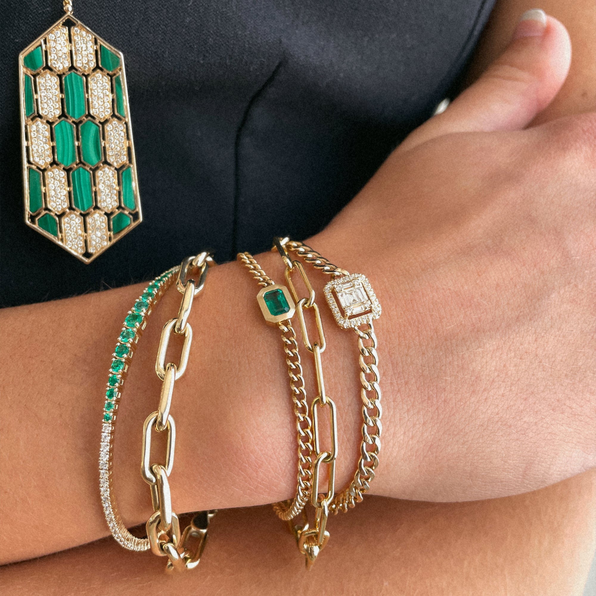 Close up of arm wearing the Emerald Bracelet, the Eternity Bracelet, the Timeless Bracelet, the Emerald Diamond Flexible Bangle, and the Halo Illusion Bracelet