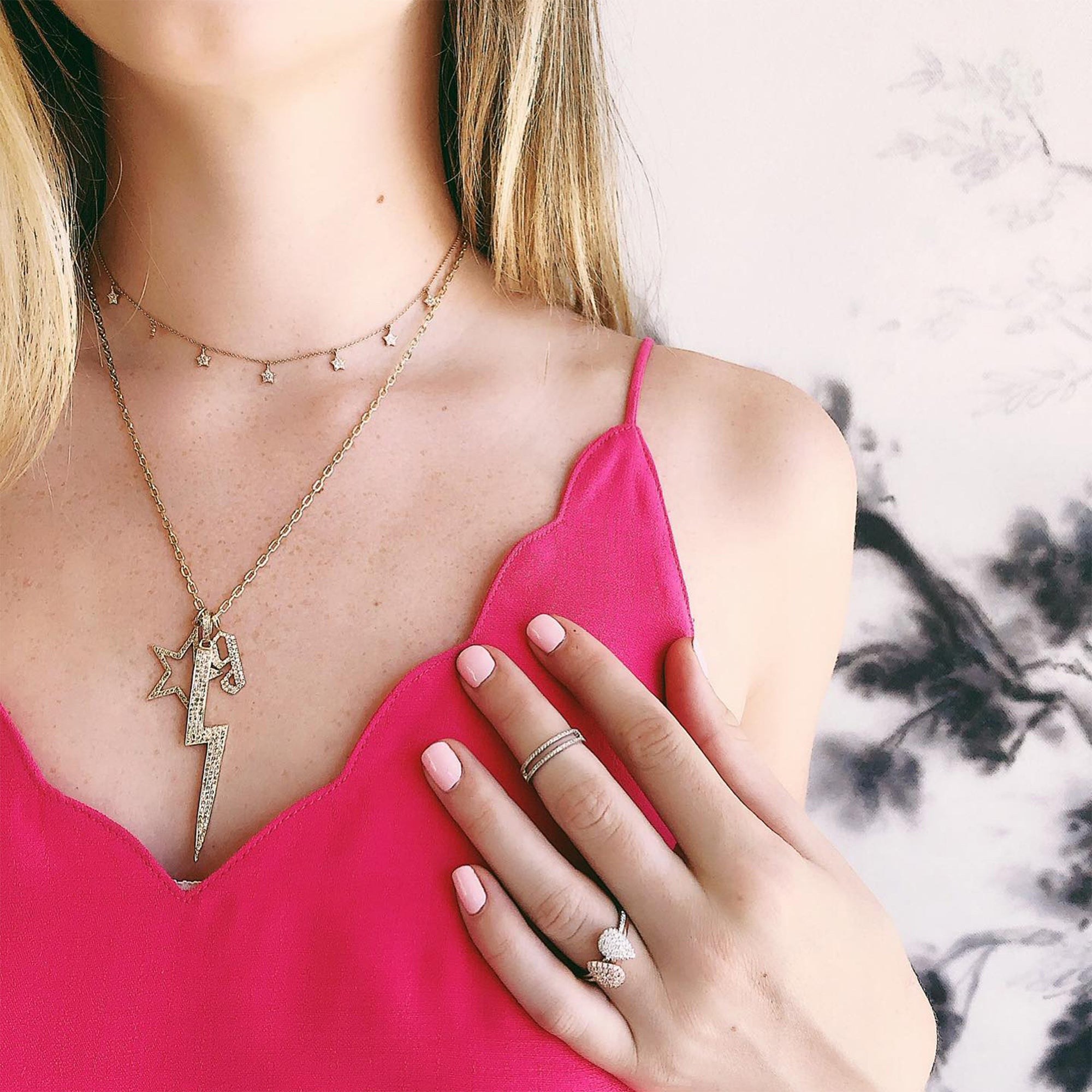 woman wearing a charm necklace with the Hollow Diamond Star Pendant, the Large Lightning Pendant, and the 'g' Small White Diamond Alphabet Pendant,  the Diamond Teardrop Ring w/ Gray Diamonds, and the Diamond Teardrop Ring w/ White Diamonds