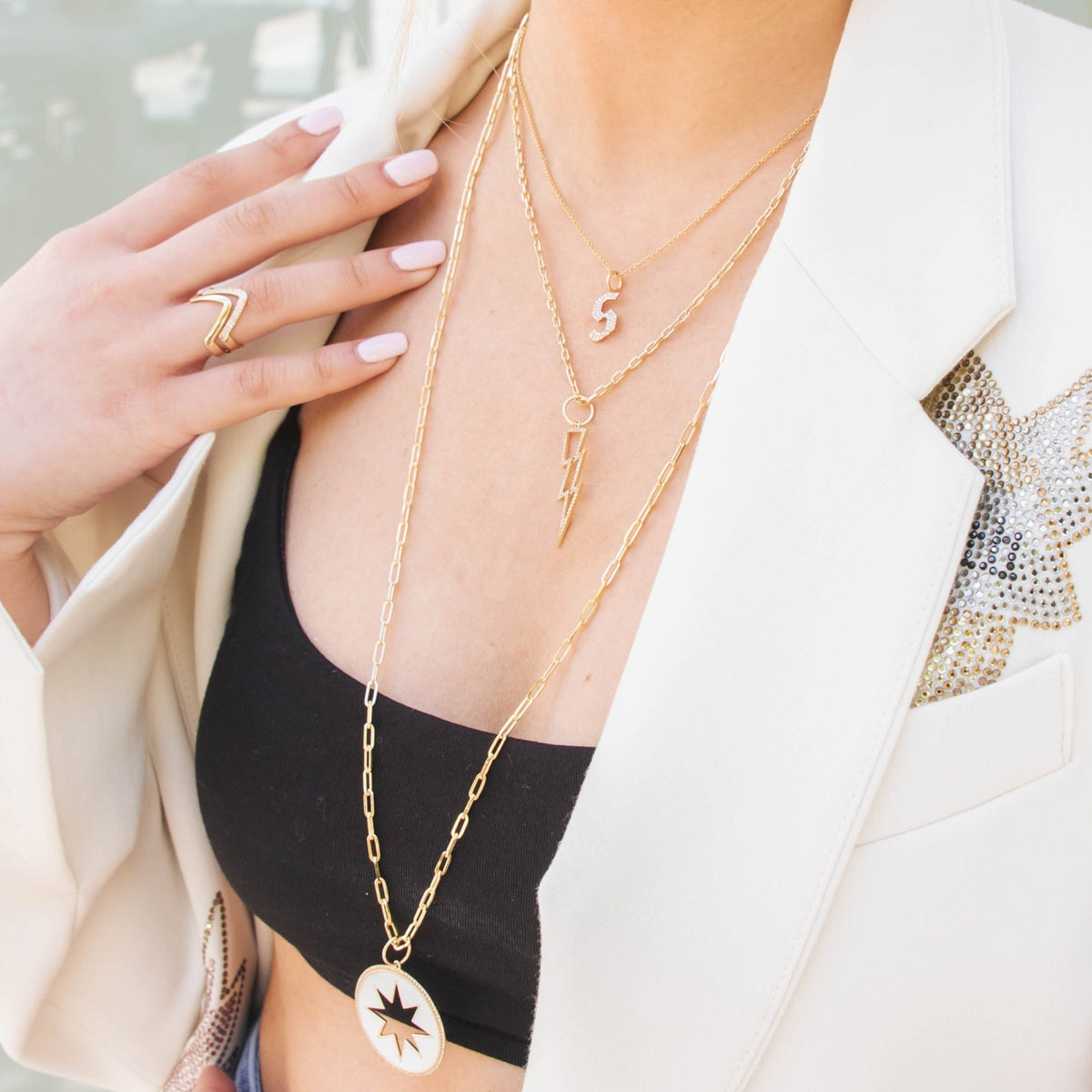 Woman wearing the Hollow Lightning Bolt Necklace, the 's' Small White Diamond Alphabet Necklace, the Large Enamel Starburst Medallion Necklace