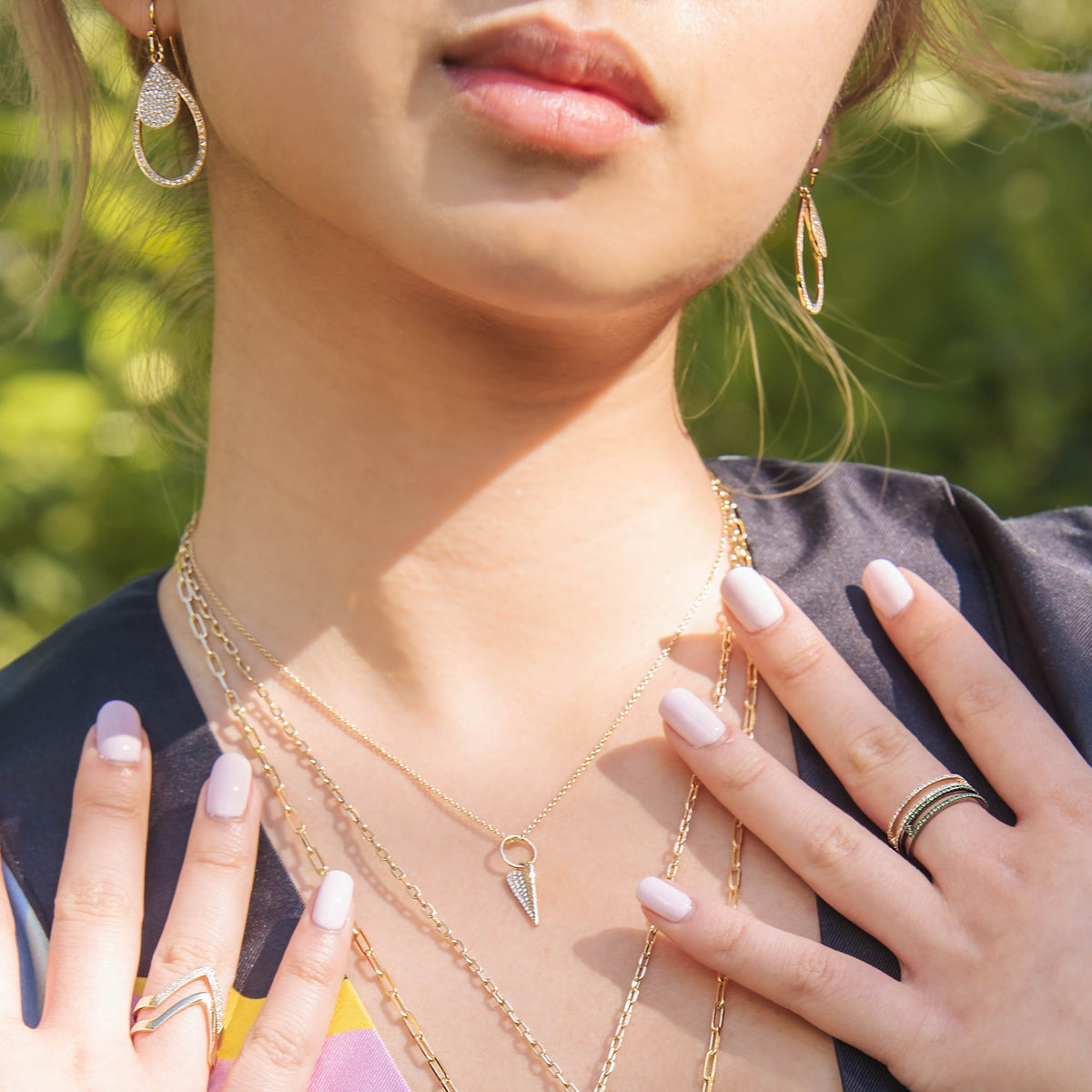 woman wearing the Mini Folded Heart Necklace, the Chevron Ring, the Green Garnet Open Bar Ring, the Mini Pave & Small Diamond Teardrops, and the Diamond Chevron Ring
