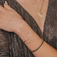 woman wearing the Open Shield Bracelet, the Shield Bracelet, Diamond 
Oval Bracelet, 2mm White and Black Diamond Stretch Bracelets, and the Diamond Dog Bone with the Small White Diamond Alphabet Necklace