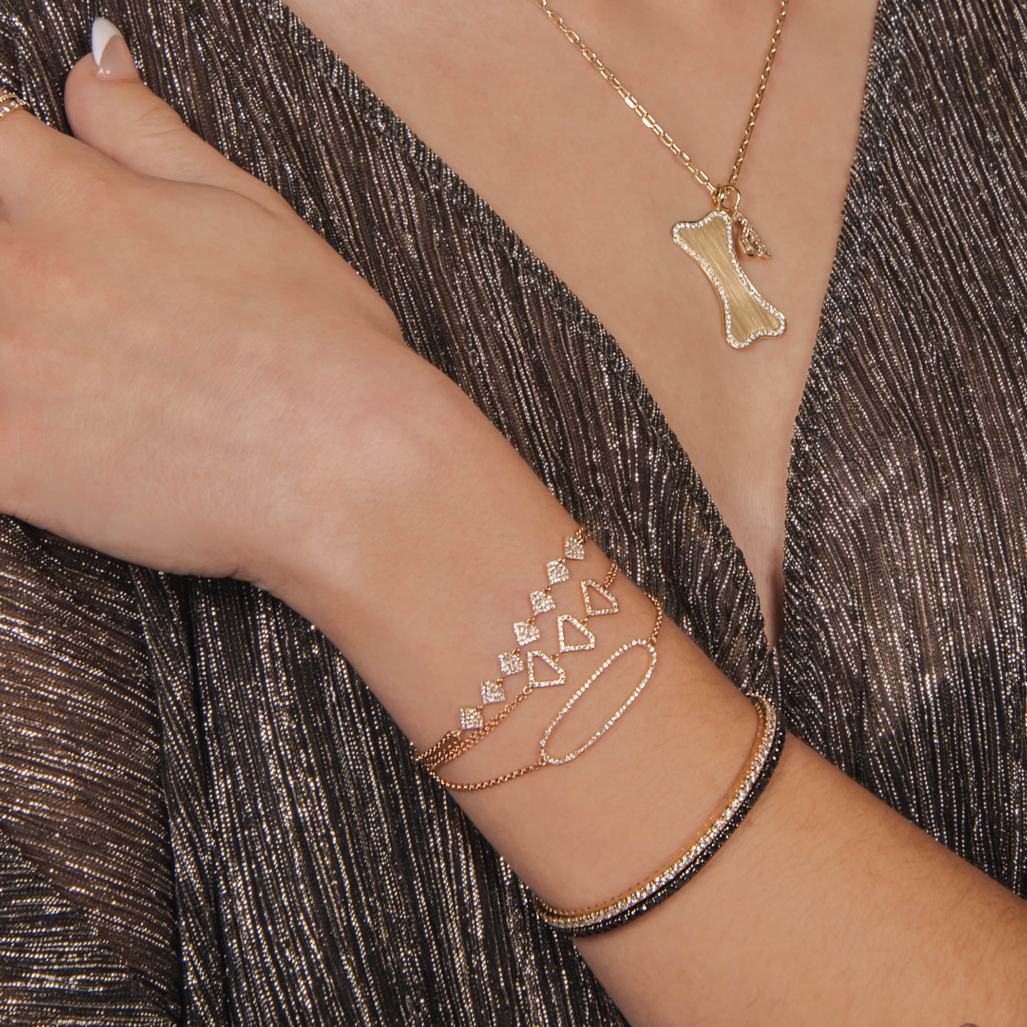 woman wearing the Open Shield Bracelet, the Shield Bracelet, Diamond 
Oval Bracelet, 2mm White and Black Diamond Stretch Bracelets, and the Diamond Dog Bone with the Small White Diamond Alphabet Necklace