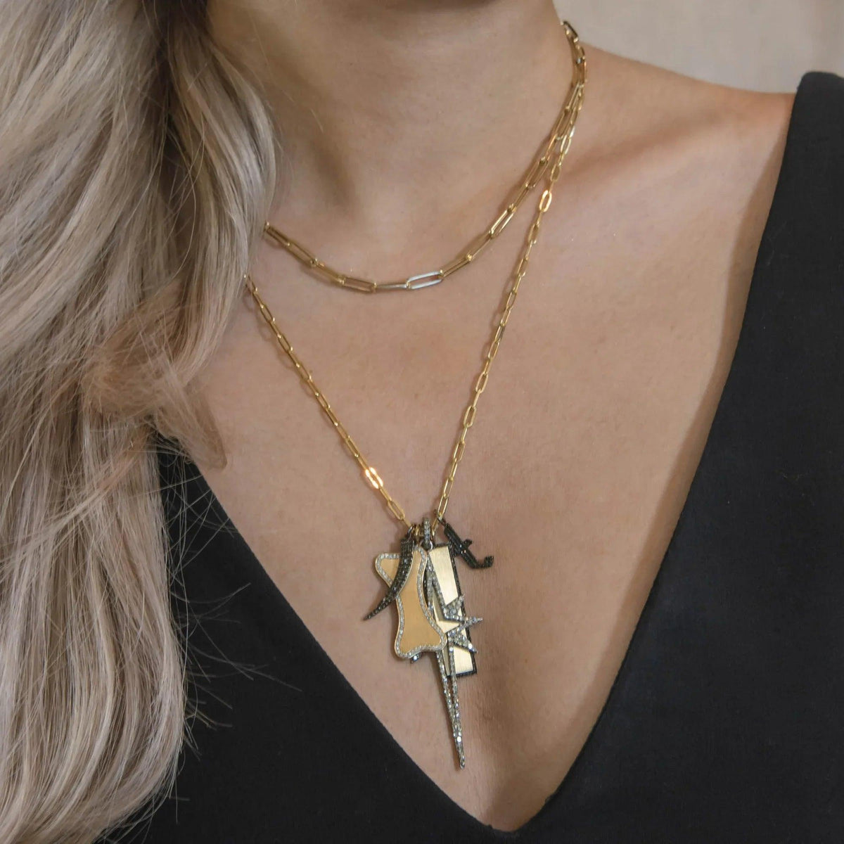 The woman is wearing the Timeless Necklace and a charm necklace that includes the Black Diamond Tusk Pendant, the Large Diamond Dog Bone, the Large Starburst Spear Pendant, the Small Black Diamond  Alphabet Pendant, and the Black Diamond Dog Tag